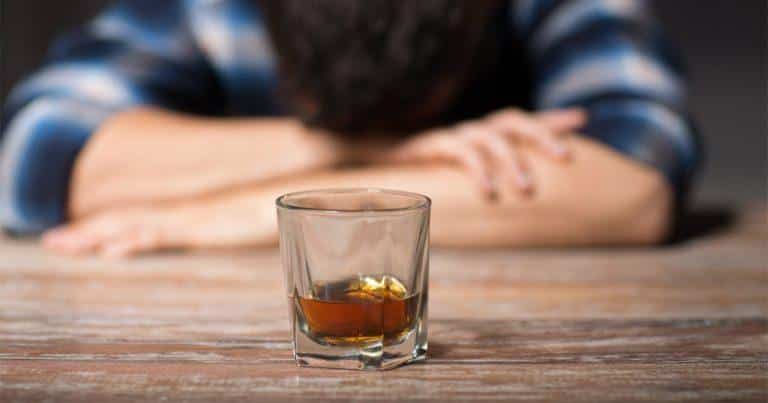 Alcohol Addiction & Withdrawal - Man face down at a table with a shot glass filled with alcohol