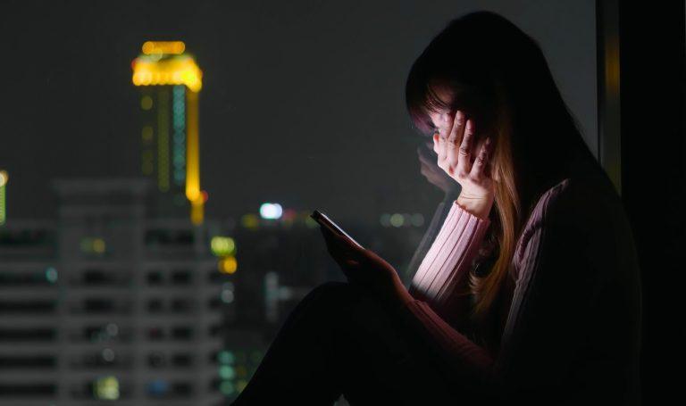 A young woman watches a TikTox #DetoxDiaries video on her smartphone.